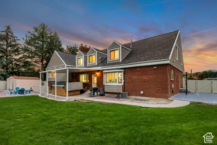 Expansive backyard featuring a manicured lawn, brick exterior, covered patio, and swim spa