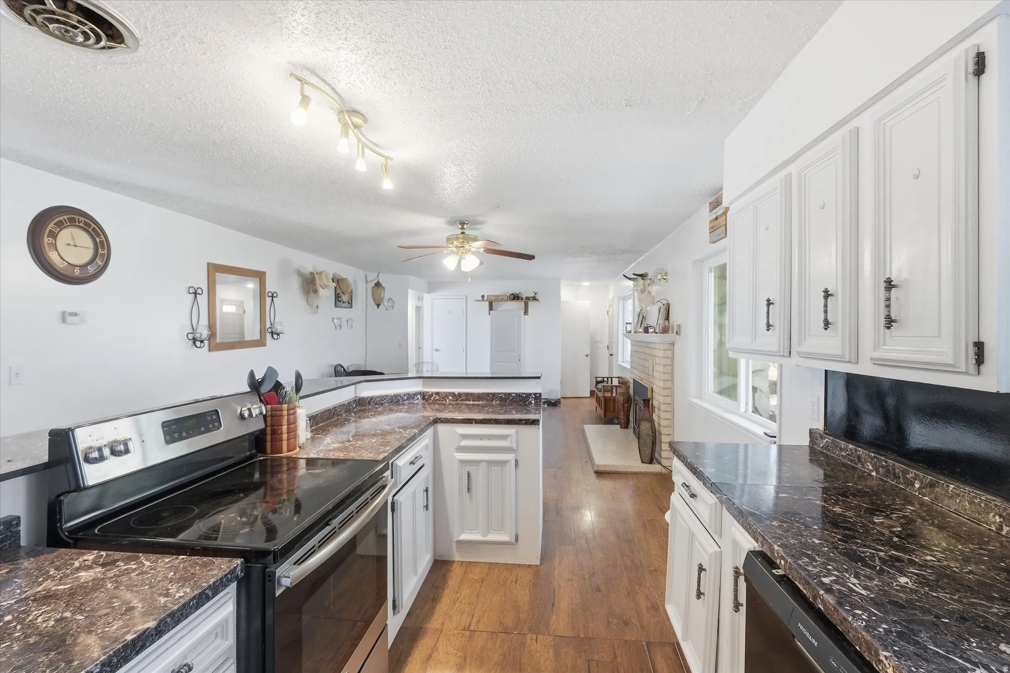 Kitchen featuring stainless steel range with electric stovetop, white cabinets, ceiling fan, dishwashing machine, and a textured ceiling
