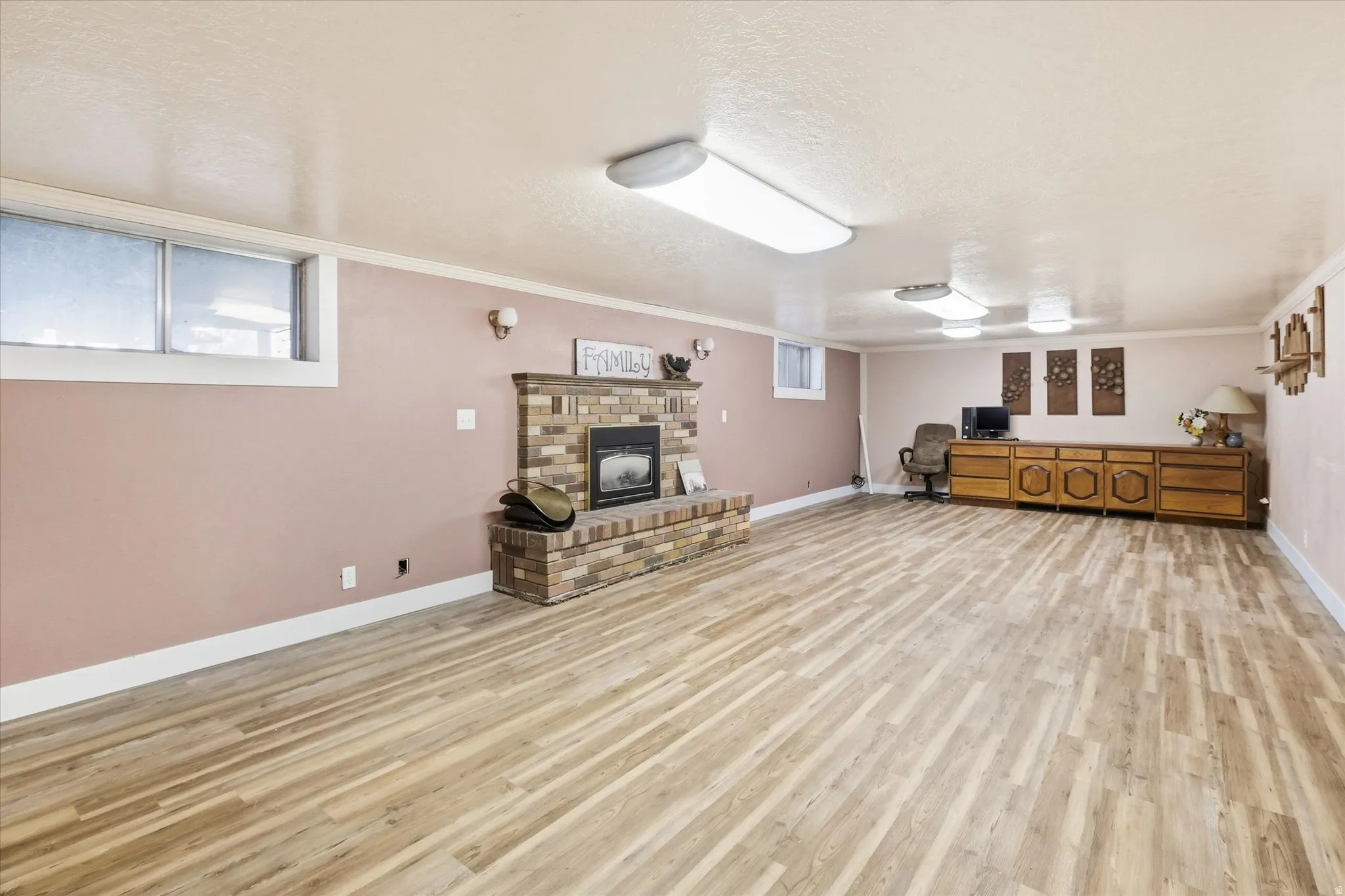 Living area featuring a textured ceiling, light wood-style floors, a fireplace, and ornamental molding