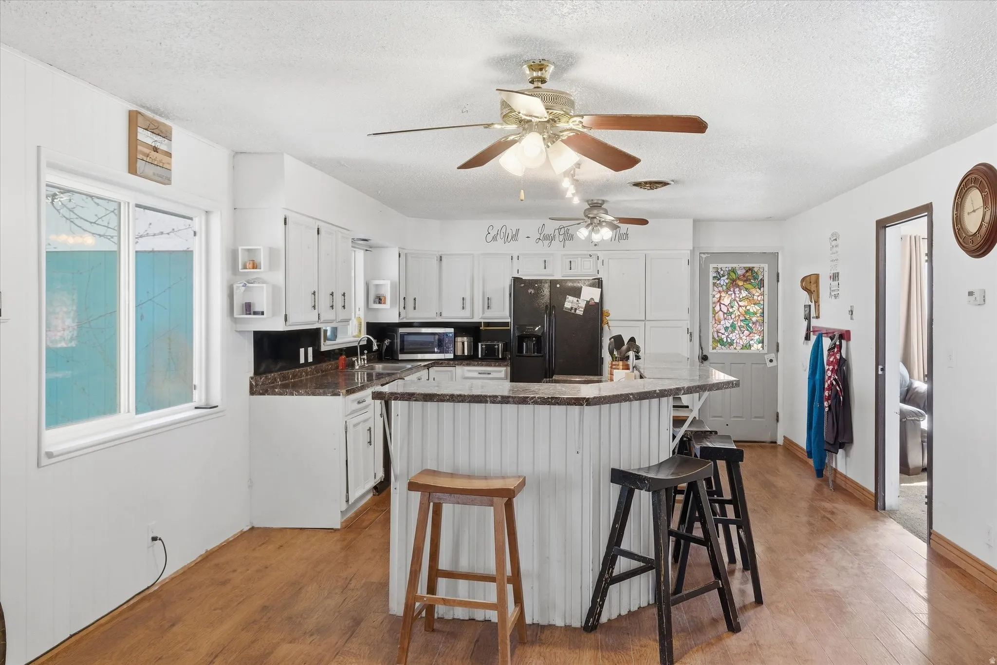Kitchen with light wood-style floors, black refrigerator with ice dispenser, white cabinetry, open shelves, and a kitchen island