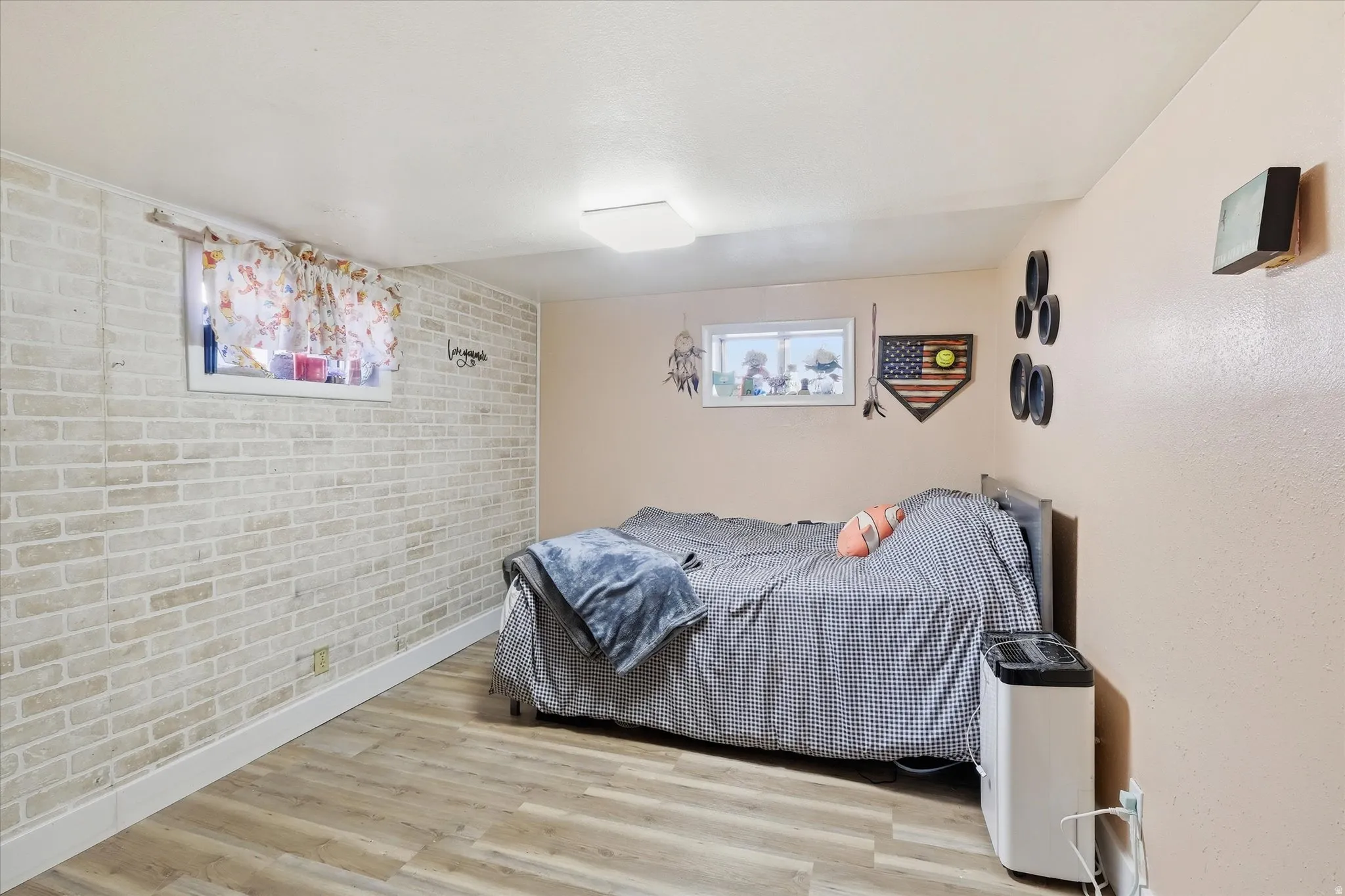 Bedroom 4 in basement featuring brick wall, light wood-type flooring, and an accent wall