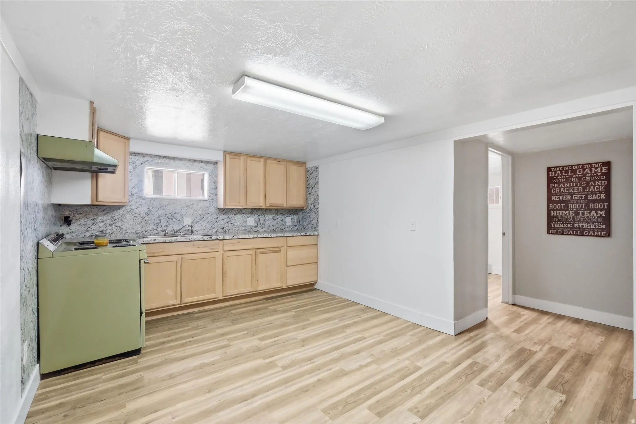 Kitchen featuring stove, light wood finish cabinetry, decorative backsplash, light wood finished floors, and light countertops