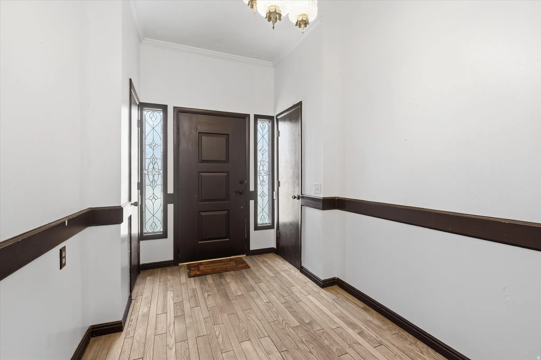 Foyer with light wood finished floors, crown molding, healthy amount of natural light, and hanging lights