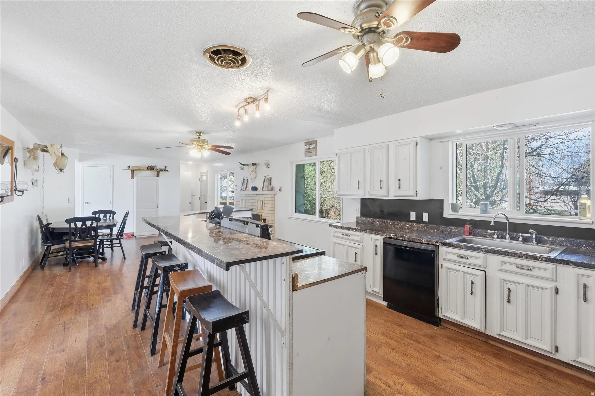 Kitchen with ceiling fan, dark countertops, a breakfast bar, white cabinetry, and black dishwasher