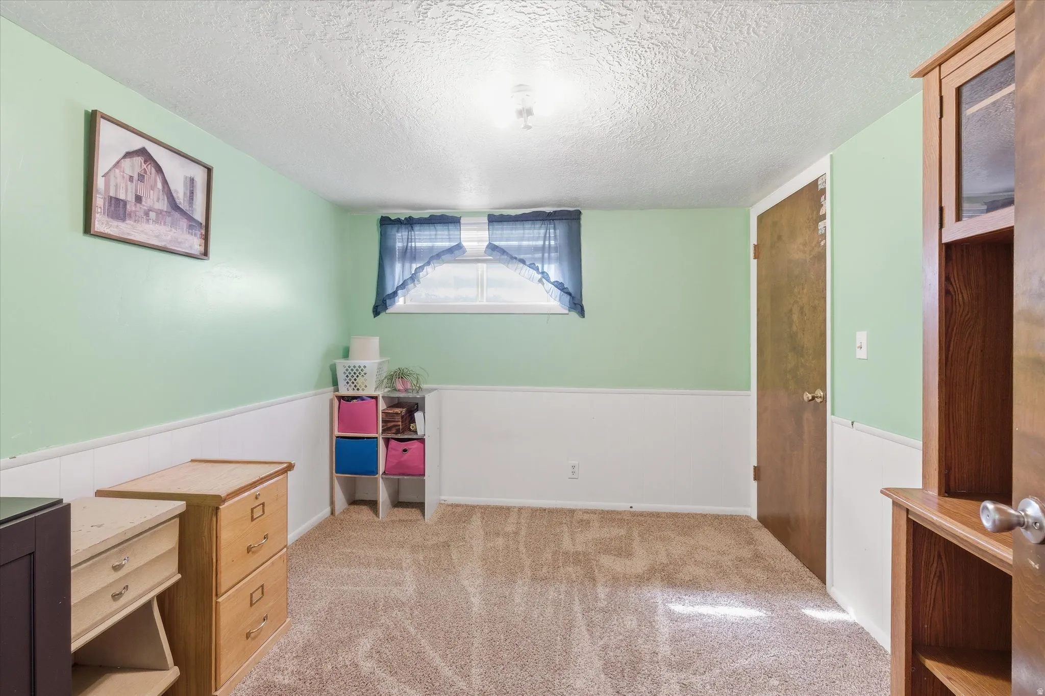 Bedroom 2 in basement featuring light colored carpet, a textured ceiling, and a wainscoted wall