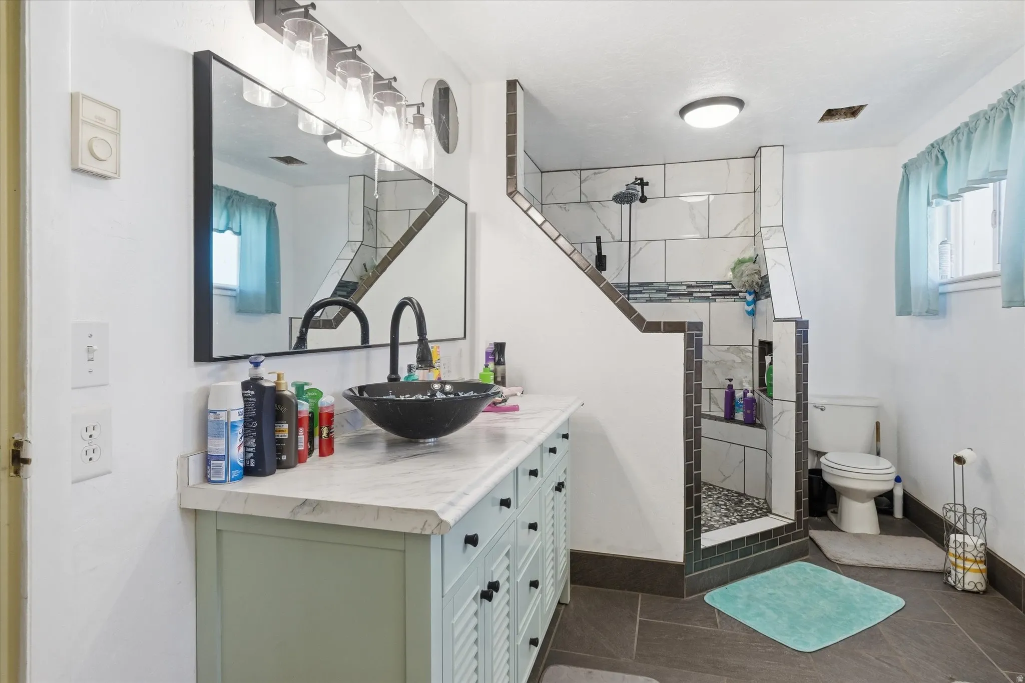 Bathroom featuring vanity, a walk in shower, and dark tile patterned flooring