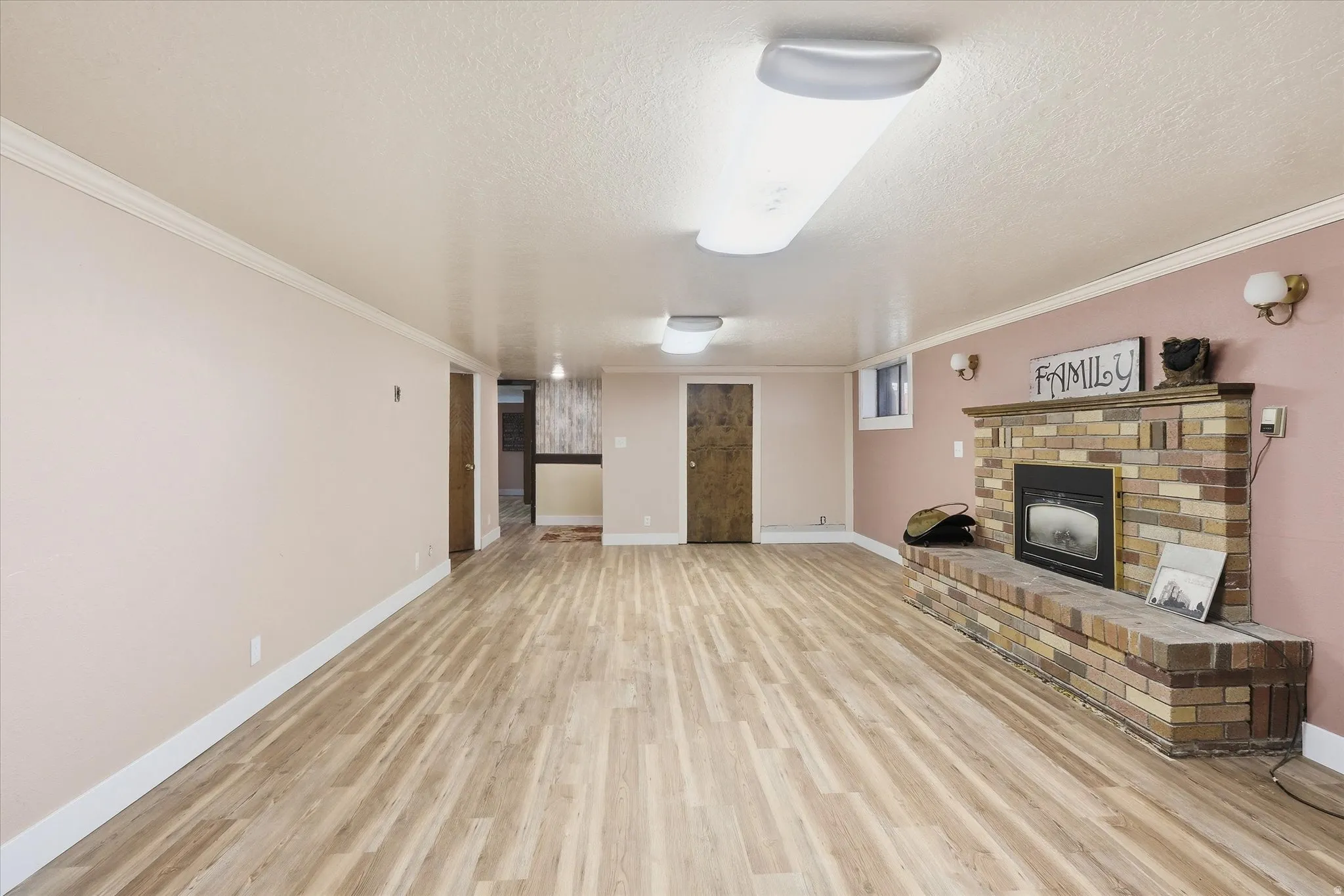 Unfurnished living room featuring a fireplace, light wood-style flooring, crown molding, and a textured ceiling