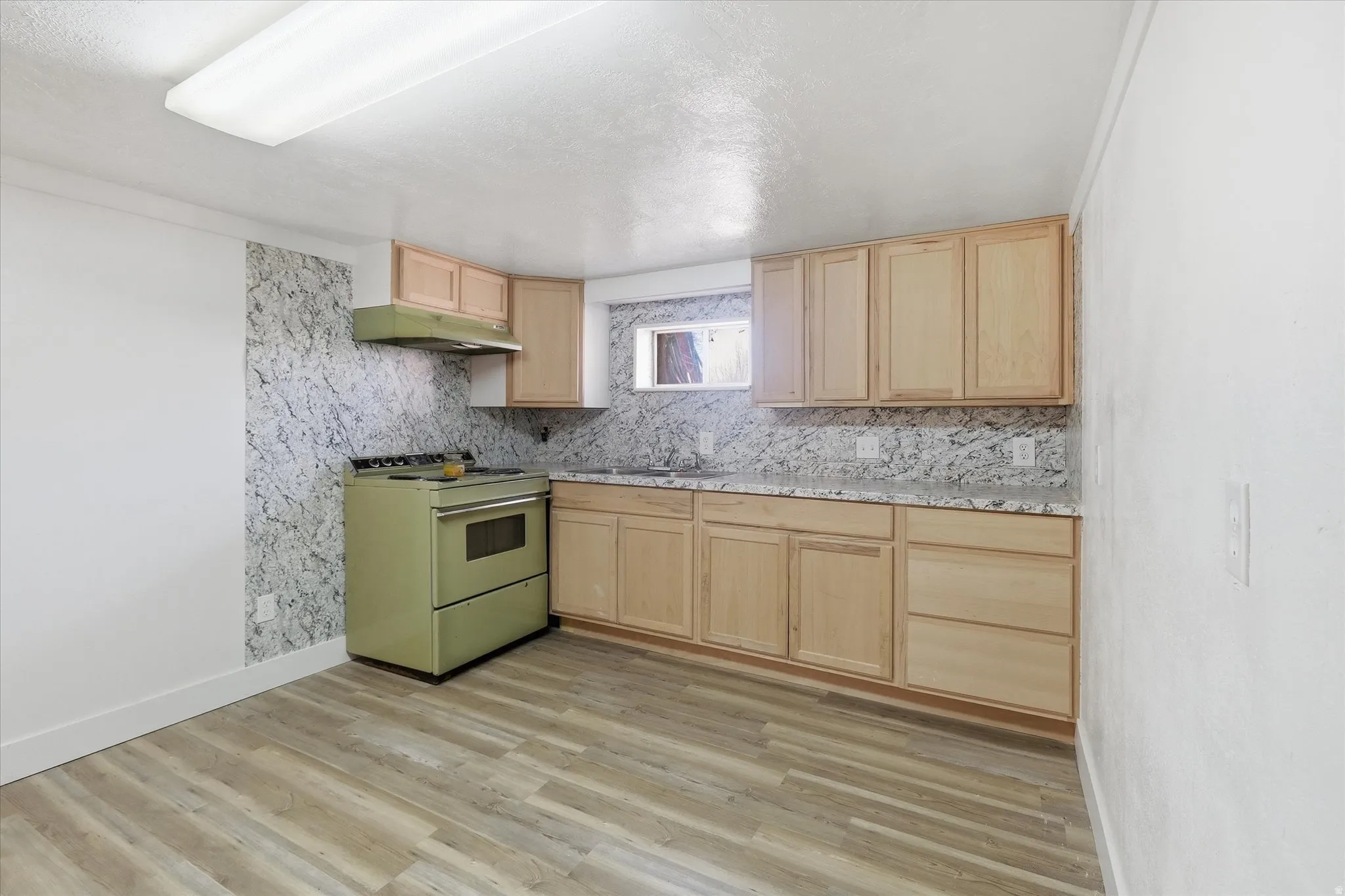 Kitchen with light wood finish cabinets, electric range, light wood finished floors, tasteful backsplash, and light countertops