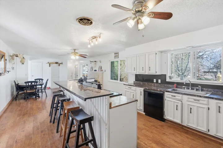 Kitchen with ceiling fan, dark countertops, a breakfast bar, white cabinetry, and black dishwasher