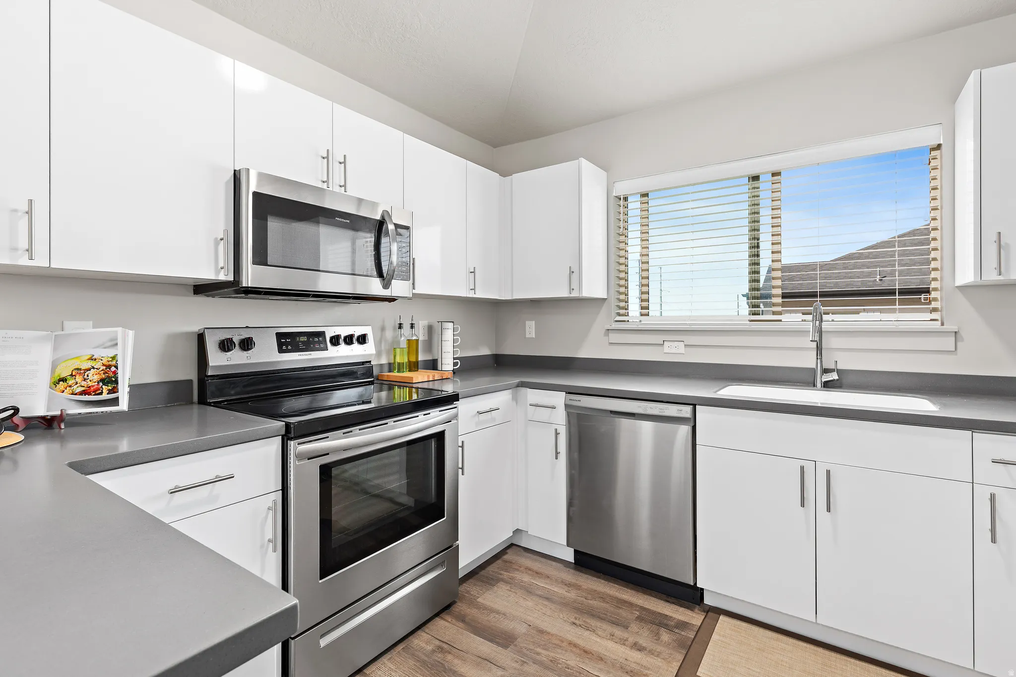 Kitchen with stainless steel appliances, white cabinets, dark countertops, wood-style floors, and lofted ceiling and Lake Views.