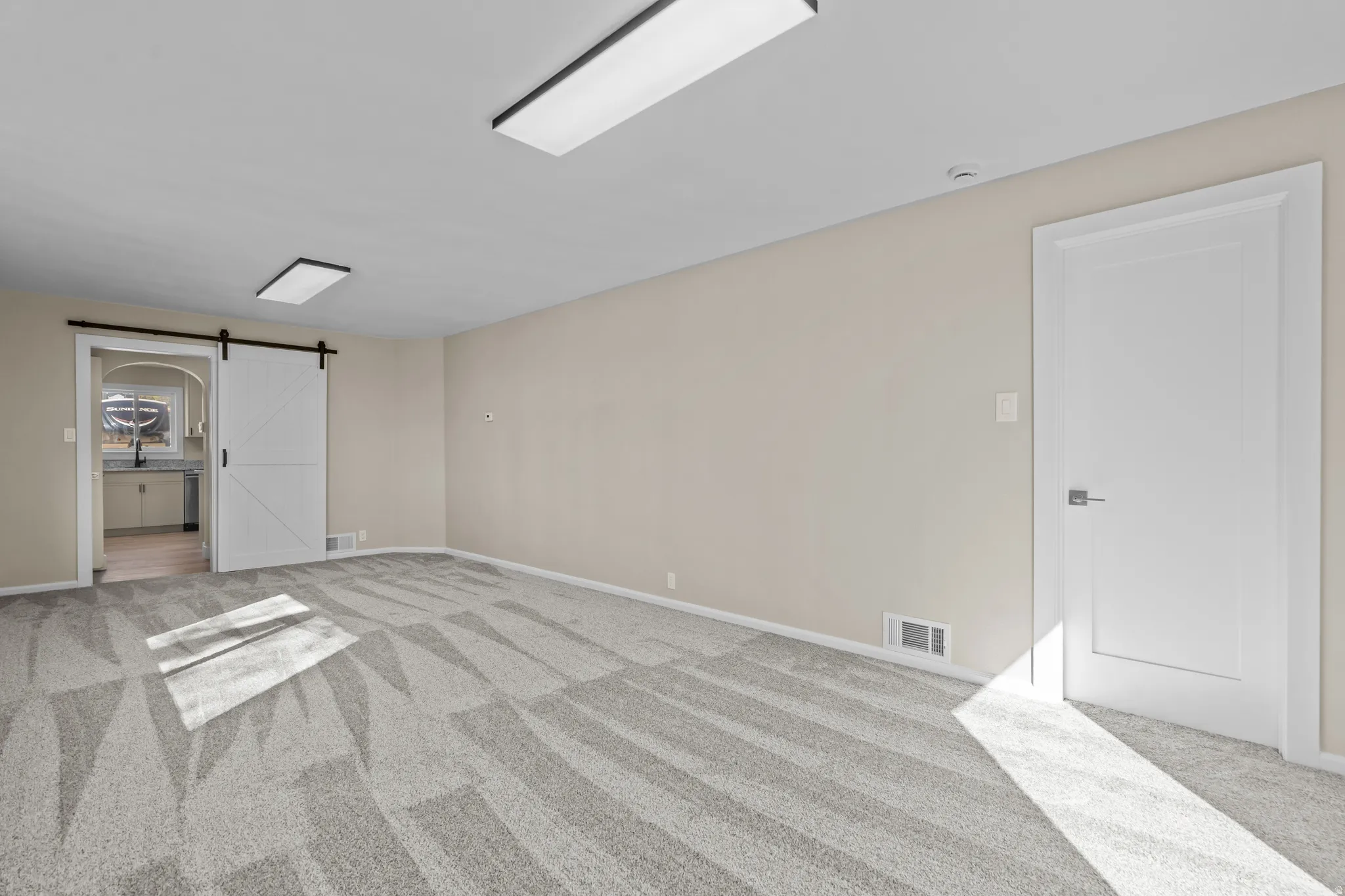 Unfurnished bedroom with a barn door, light carpet, and ensuite bath