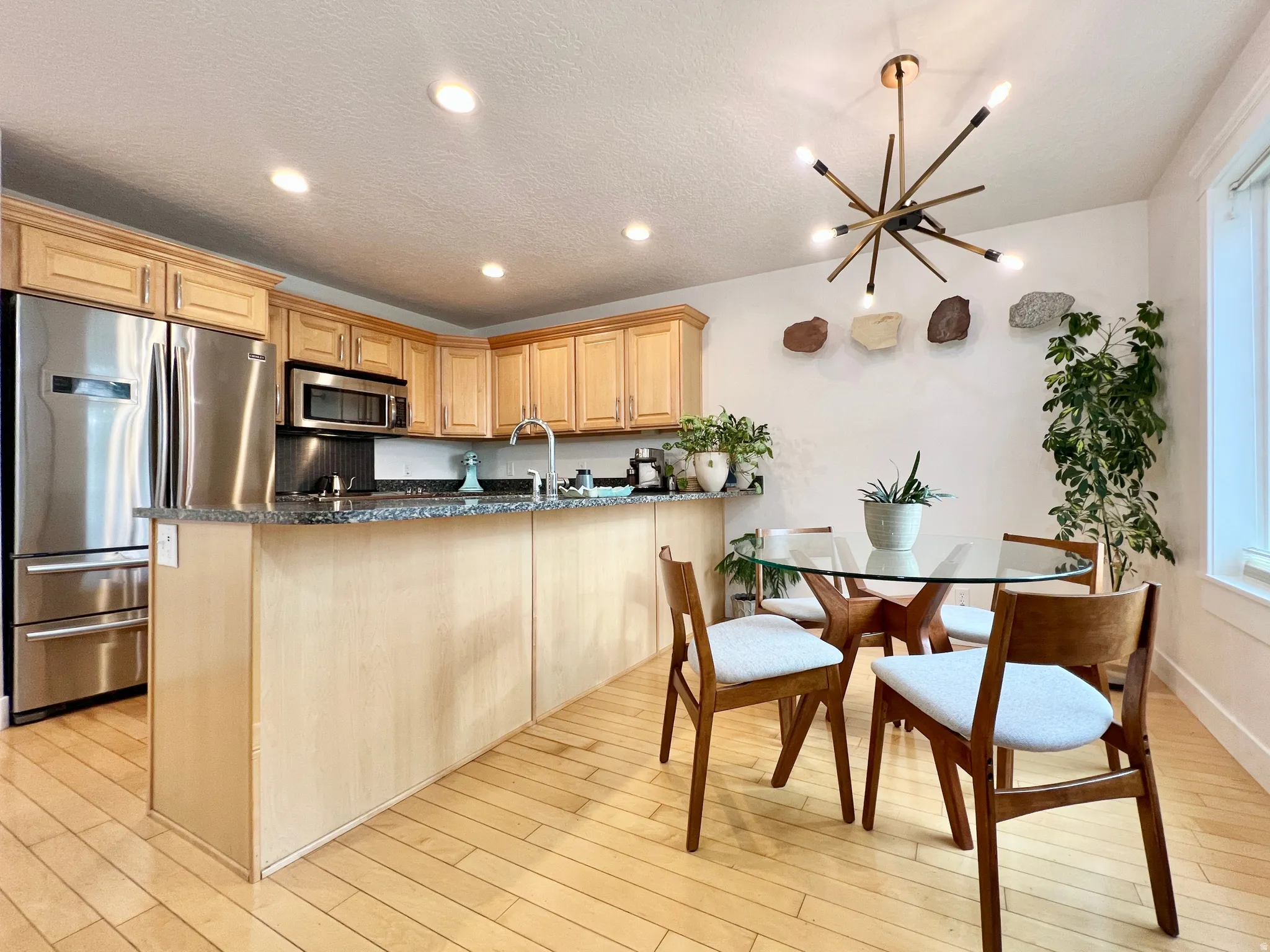 Kitchen featuring stainless steel appliances, a peninsula, dark stone countertops, light wood finish cabinets, and light wood finished floors