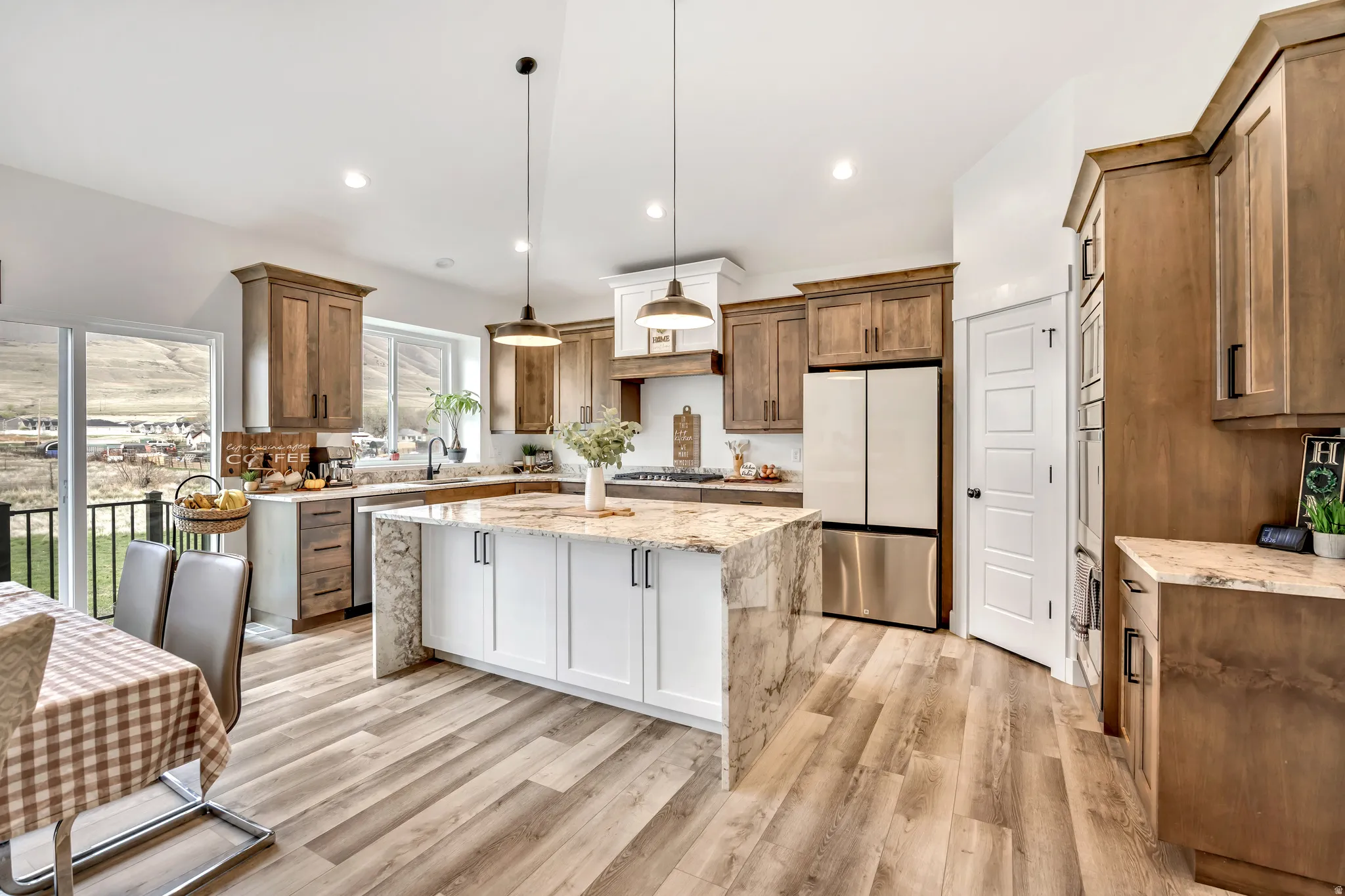 Kitchen with light stone counters, freestanding refrigerator, a center island, light wood-style floors, and hanging light fixtures