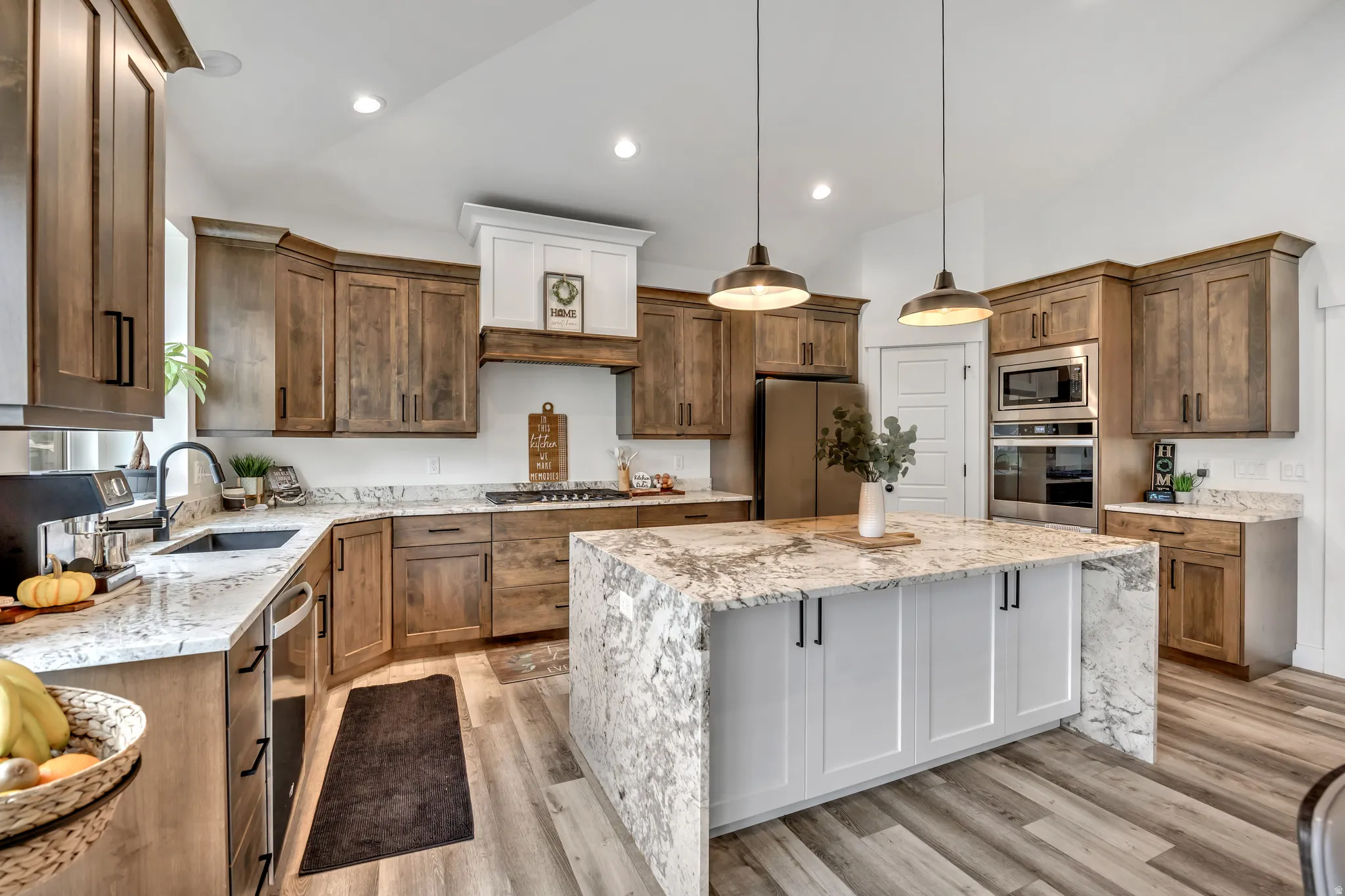 Kitchen featuring light stone countertops, vaulted ceiling, hanging light fixtures, stainless steel appliances, and light wood-style floors