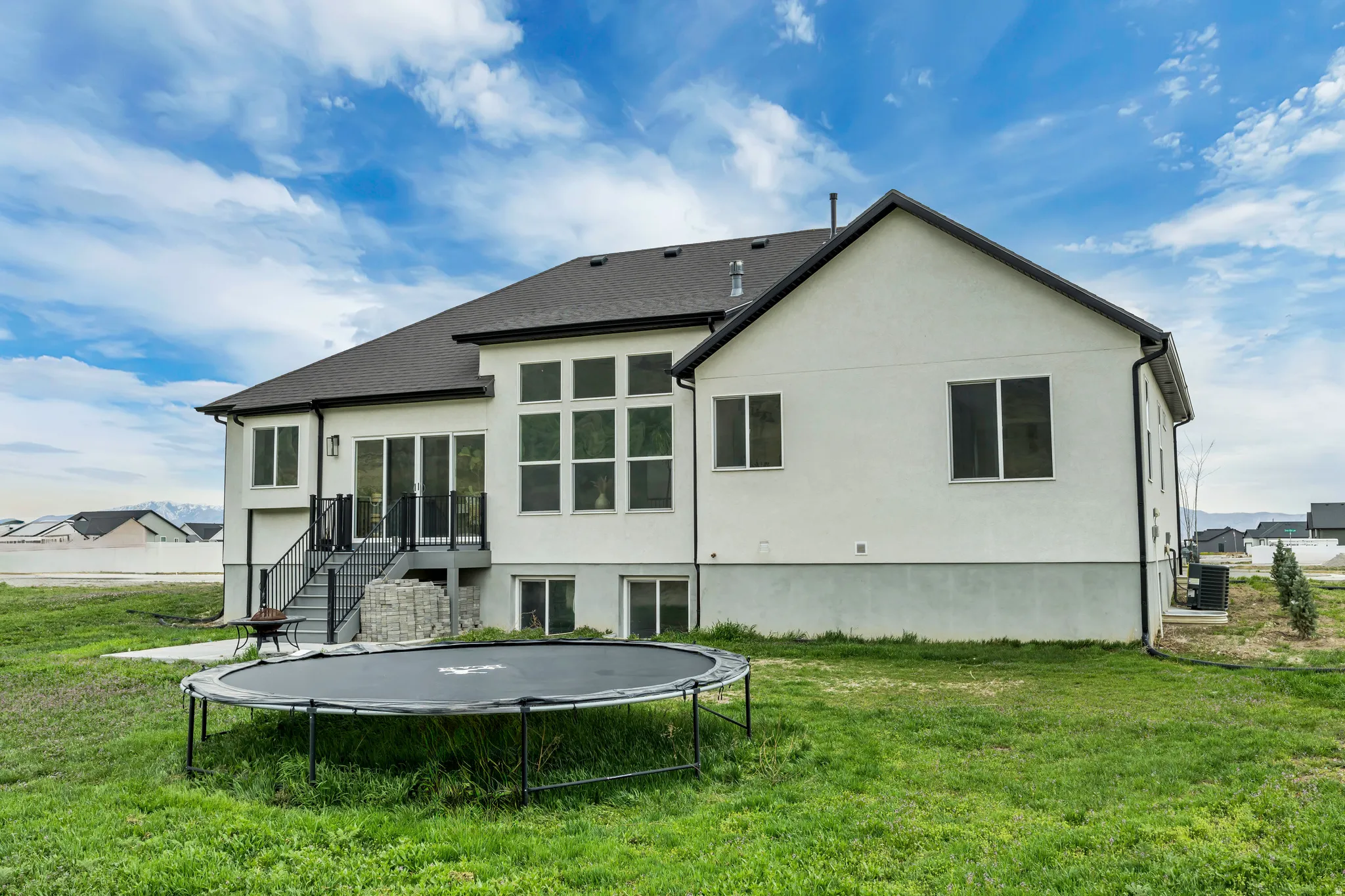 Rear view of property with a trampoline, a yard, stucco siding, and a patio