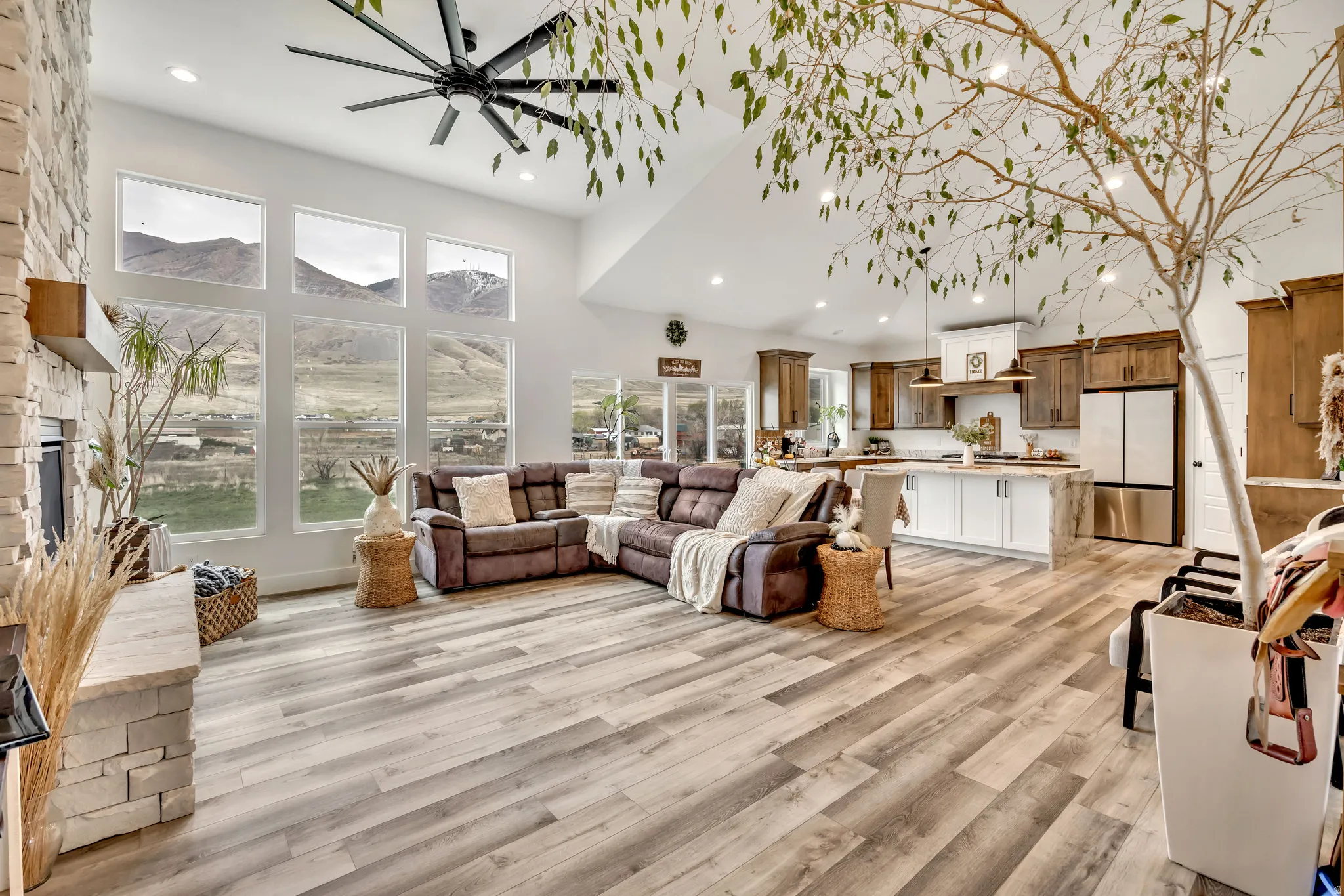 Living area featuring a stone fireplace, a high ceiling, a ceiling fan, light wood-style floors, and recessed lighting
