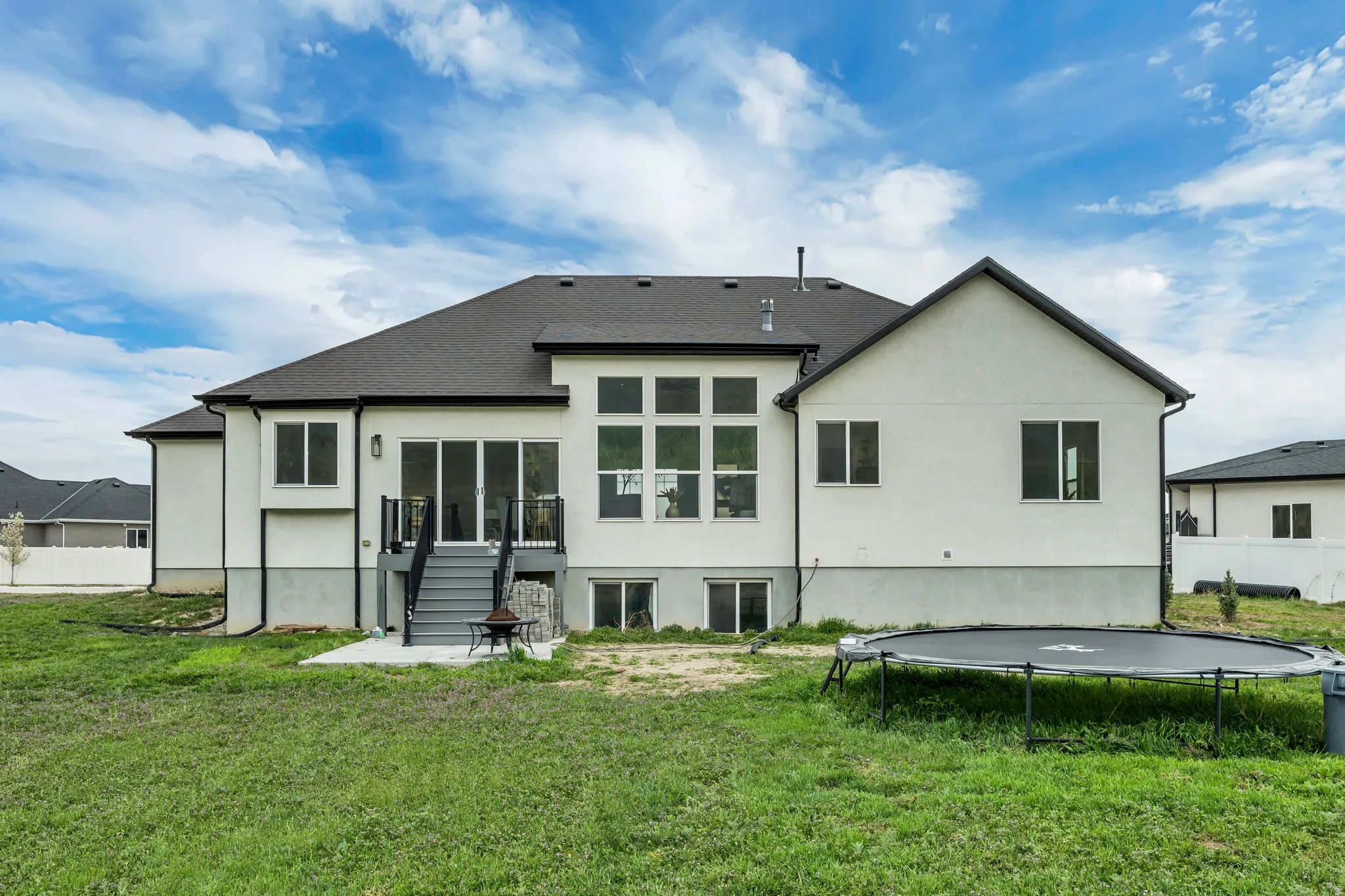 Rear view of house featuring a trampoline, a patio, stucco siding, and an outdoor fire pit