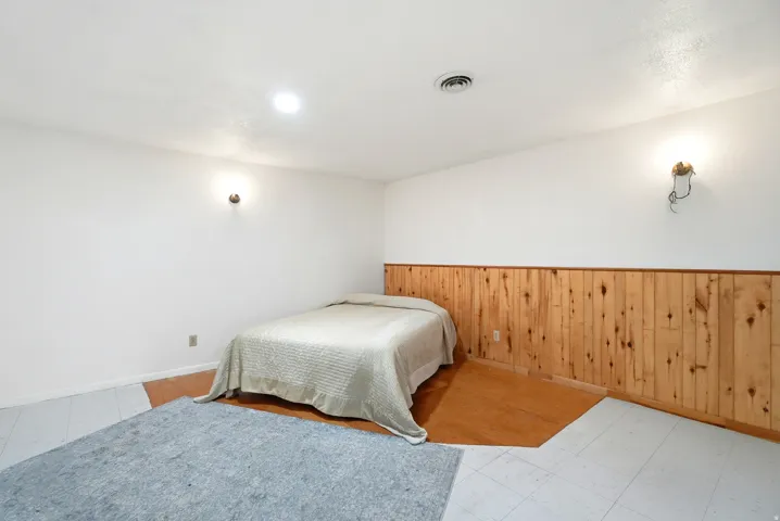 Bedroom with wooden walls, a wainscoted wall, and light flooring