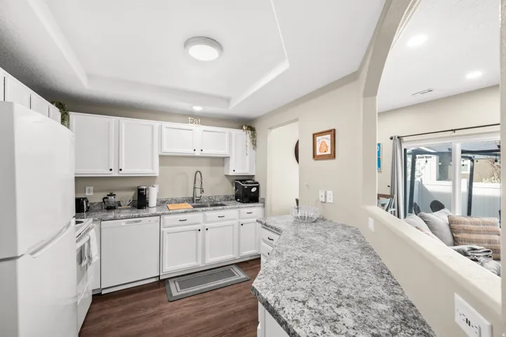 Kitchen with white cabinetry, white appliances, dark wood-style floors, arched walkways, and recessed lighting