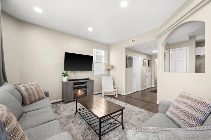 Living room with wood finished floors, arched walkways, a glass covered fireplace, and recessed lighting