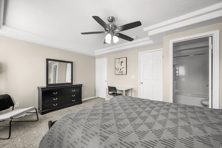 Bedroom with ensuite bath, light carpet, a raised ceiling, a ceiling fan, and a textured ceiling