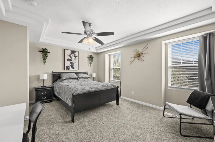 Bedroom featuring light colored carpet, a textured ceiling, ceiling fan, and a tray ceiling