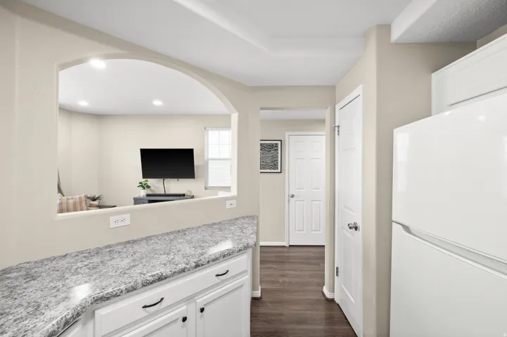 Kitchen with freestanding refrigerator, white cabinets, dark wood-style floors, and light stone counters