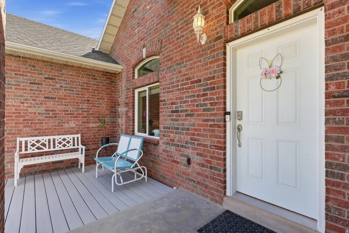 Entrance to property featuring brick siding, a deck, and a shingled roof