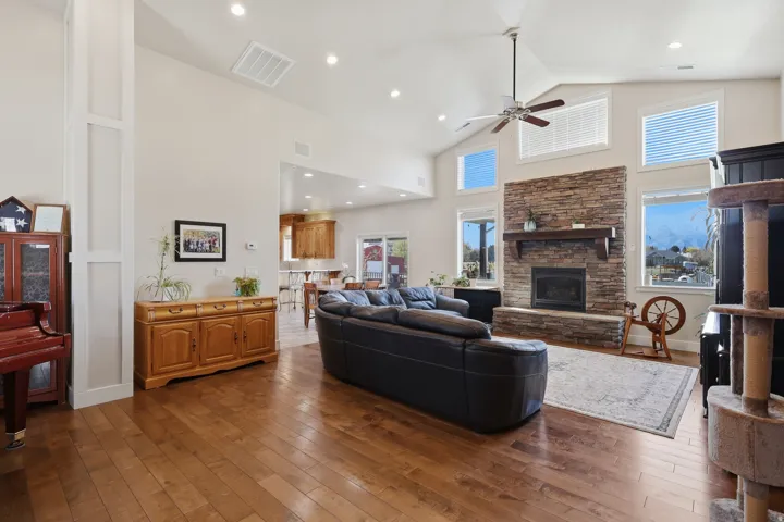 Living room featuring dark wood-style flooring, a fireplace, ceiling fan, recessed lighting, and lofted ceiling