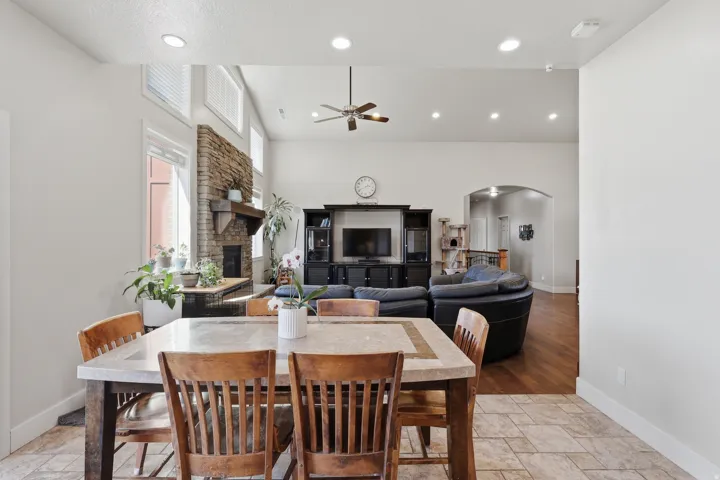 Dining space with arched walkways, stone tile flooring, a ceiling fan, a fireplace, and a high ceiling