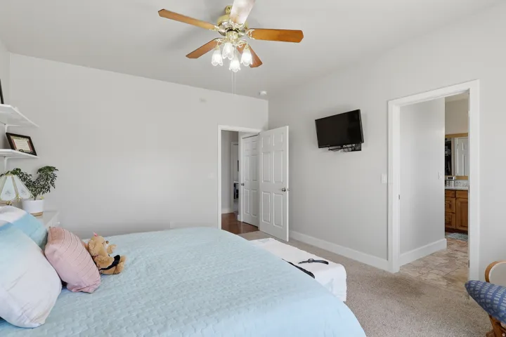Bedroom with light carpet, ensuite bath, and a ceiling fan