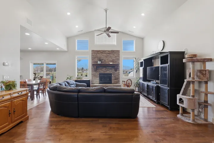 Living room with dark wood-type flooring, a high ceiling, a ceiling fan, a stone fireplace, and recessed lighting