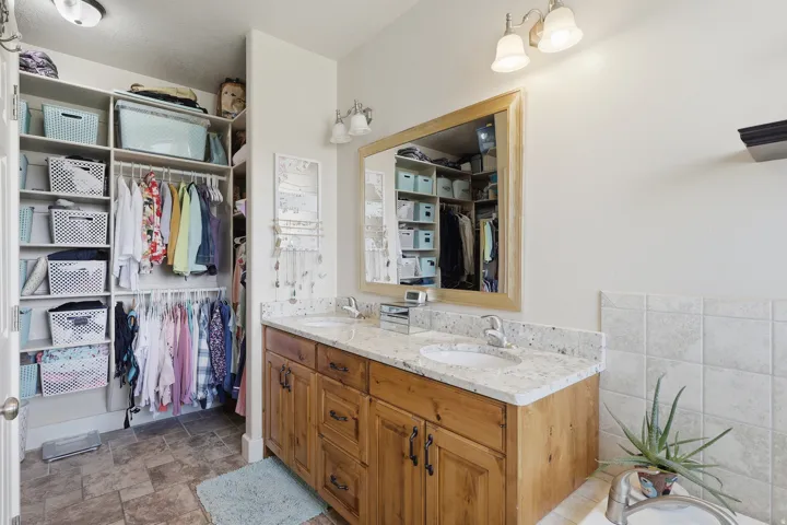 Full bathroom with double vanity, a spacious closet, stone finish floors, and a bath