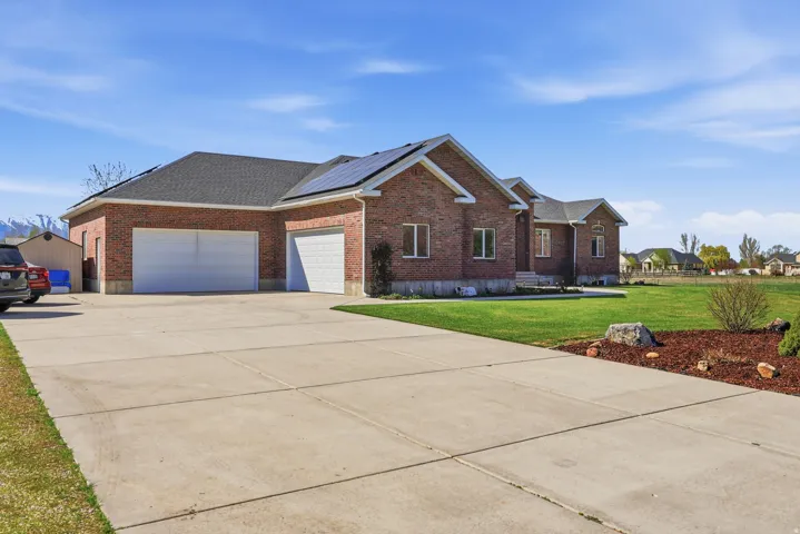 View of side of property with a garage, brick siding, a yard, solar panels, and concrete driveway