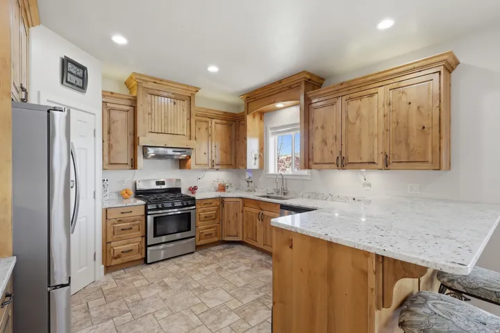 Kitchen with stainless steel appliances, a peninsula, light stone counters, a kitchen bar, and stone finish flooring