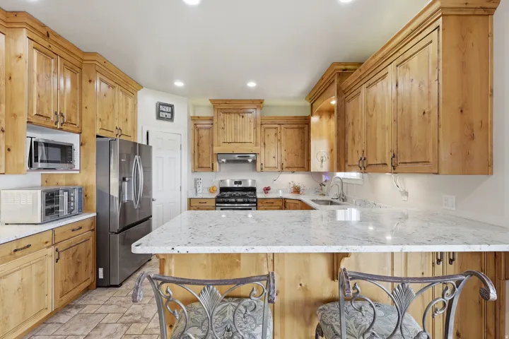 Kitchen featuring light stone countertops, stainless steel appliances, a peninsula, stone finish floors, and a breakfast bar