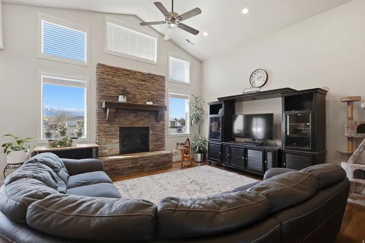 Living room featuring wood finished floors, vaulted ceiling, ceiling fan, recessed lighting, and a stone fireplace