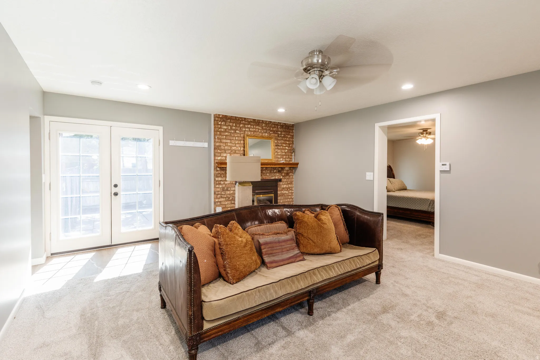 Living room featuring a ceiling fan, french doors, light colored carpet, recessed lighting, and a brick fireplace