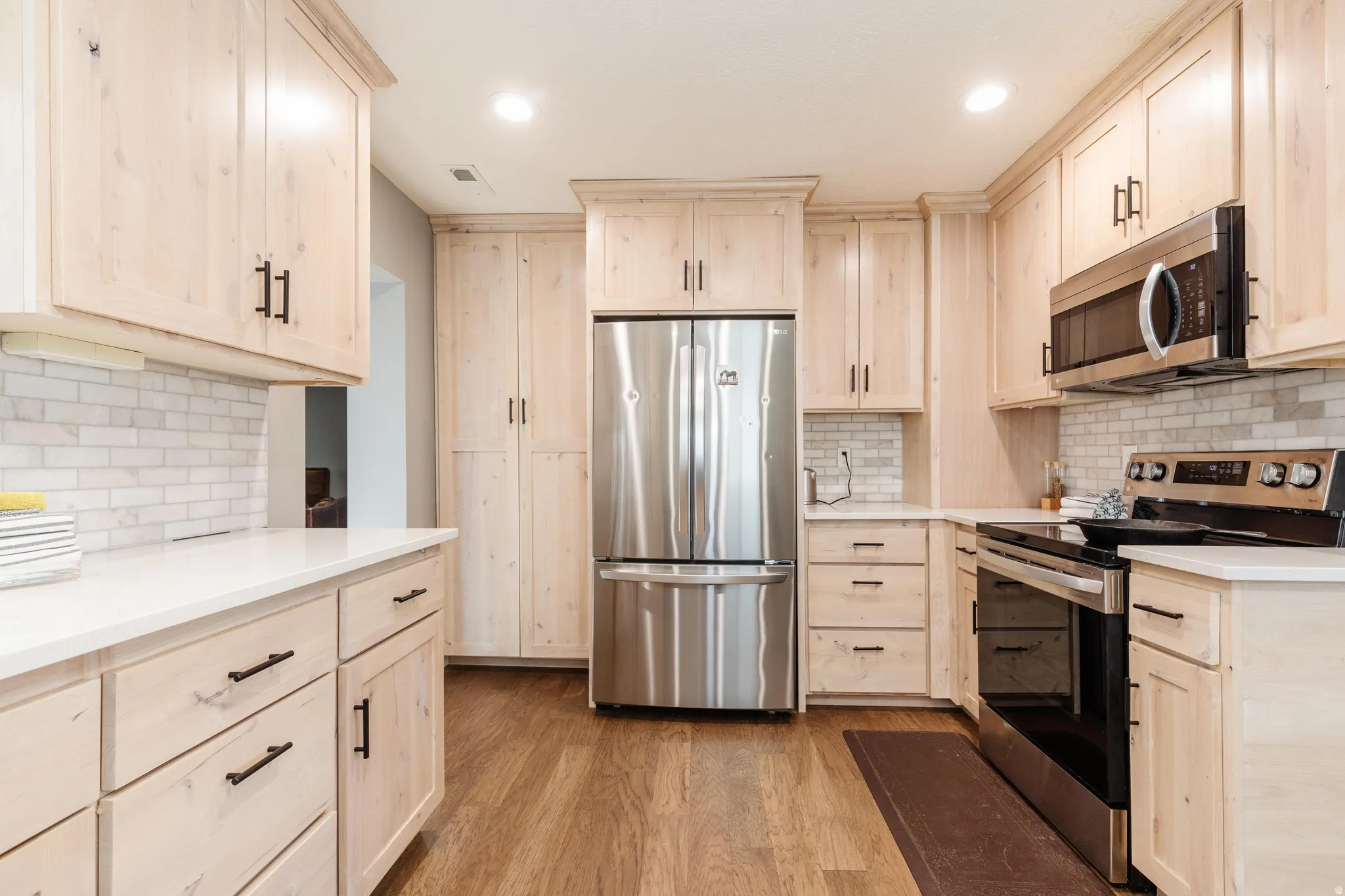Kitchen featuring stainless steel appliances, light wood-style cabinets, light stone counters, and recessed lighting