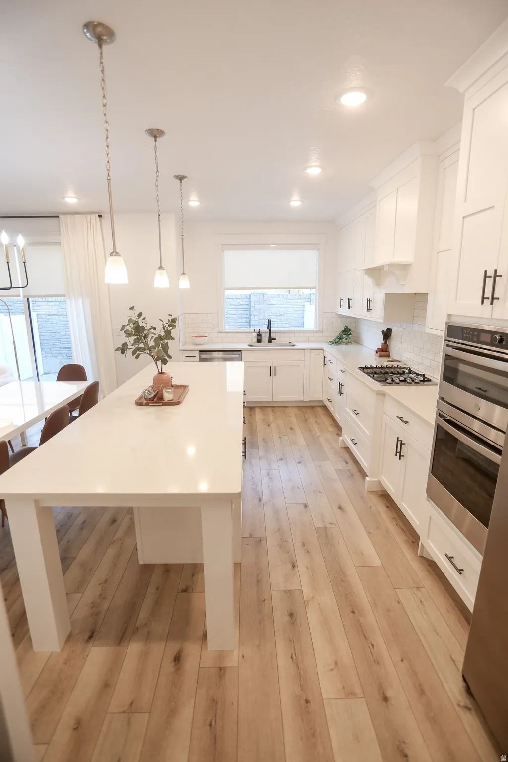 Kitchen with backsplash, stainless steel appliances, white cabinetry, hanging light fixtures, and a center island