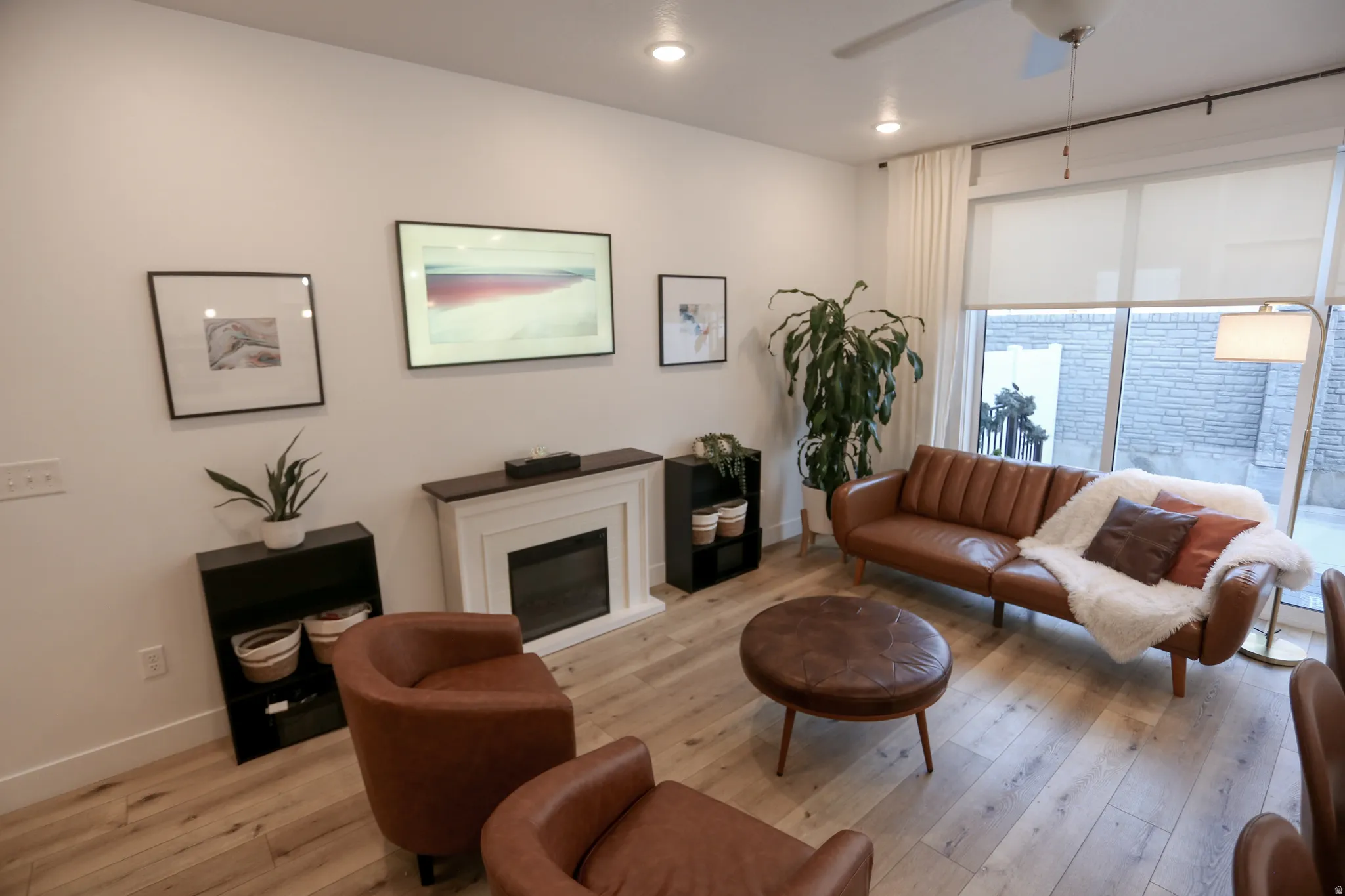 Living room with light wood-type flooring, ceiling fan, and a glass covered fireplace
