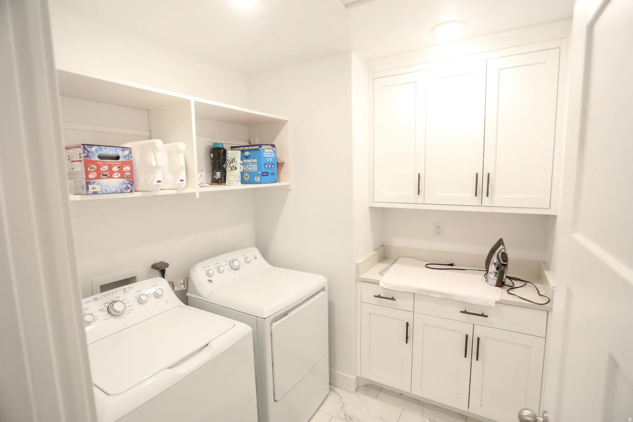Laundry area with cabinet space, light marble finish floors, and washer and dryer