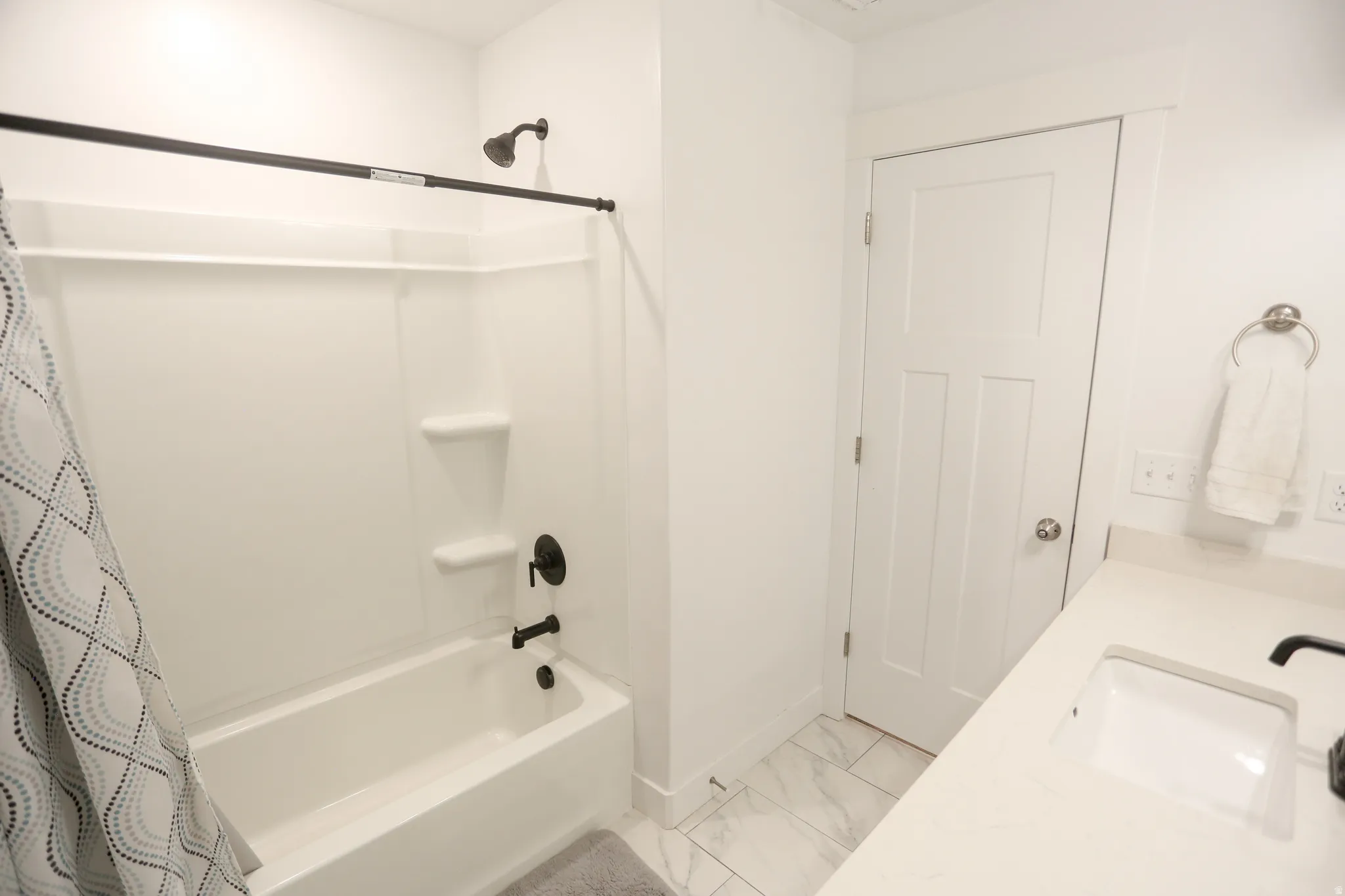 Bathroom featuring vanity, shower / bath combination with curtain, and light marble finish floors
