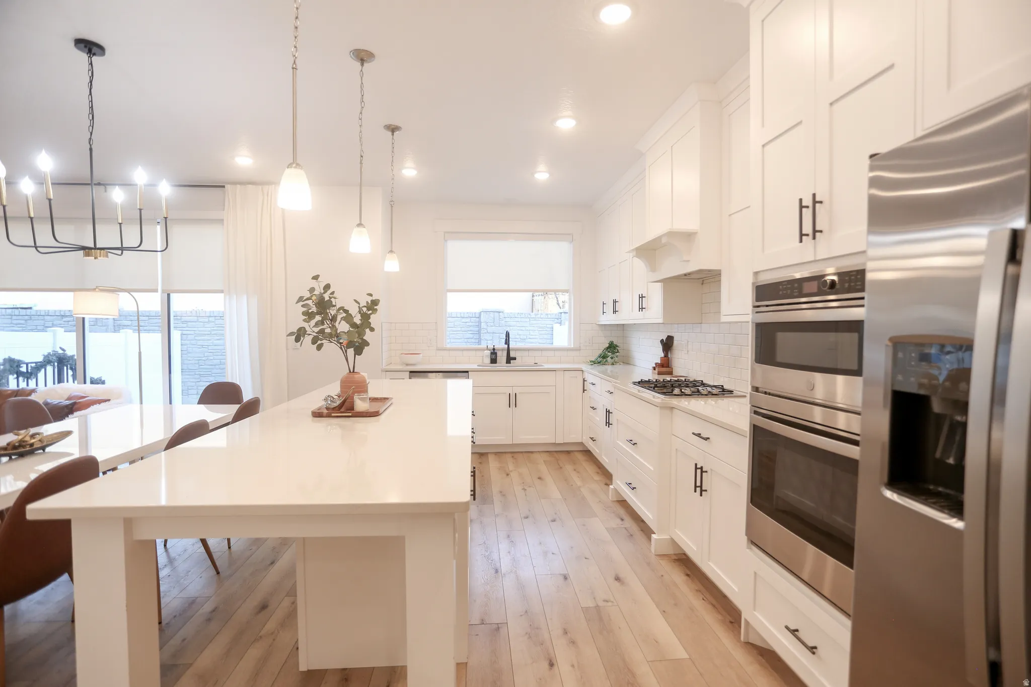 Kitchen featuring stainless steel appliances, white cabinetry, suspended lighting, a kitchen island, and backsplash