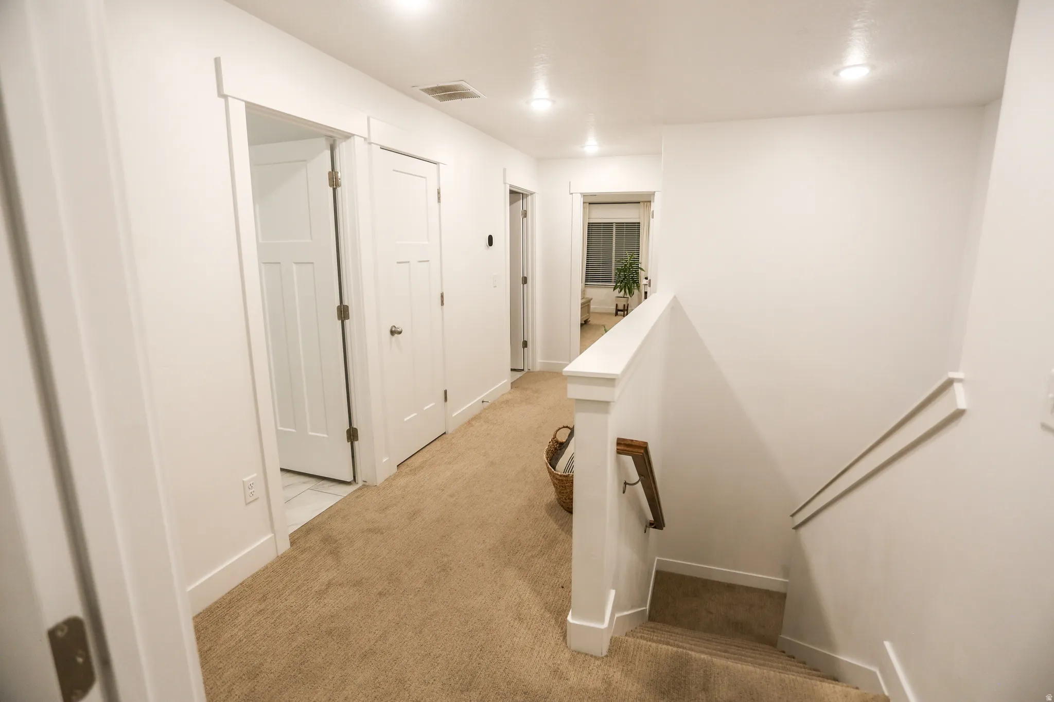 Hallway with an upstairs landing, light colored carpet, and recessed lighting