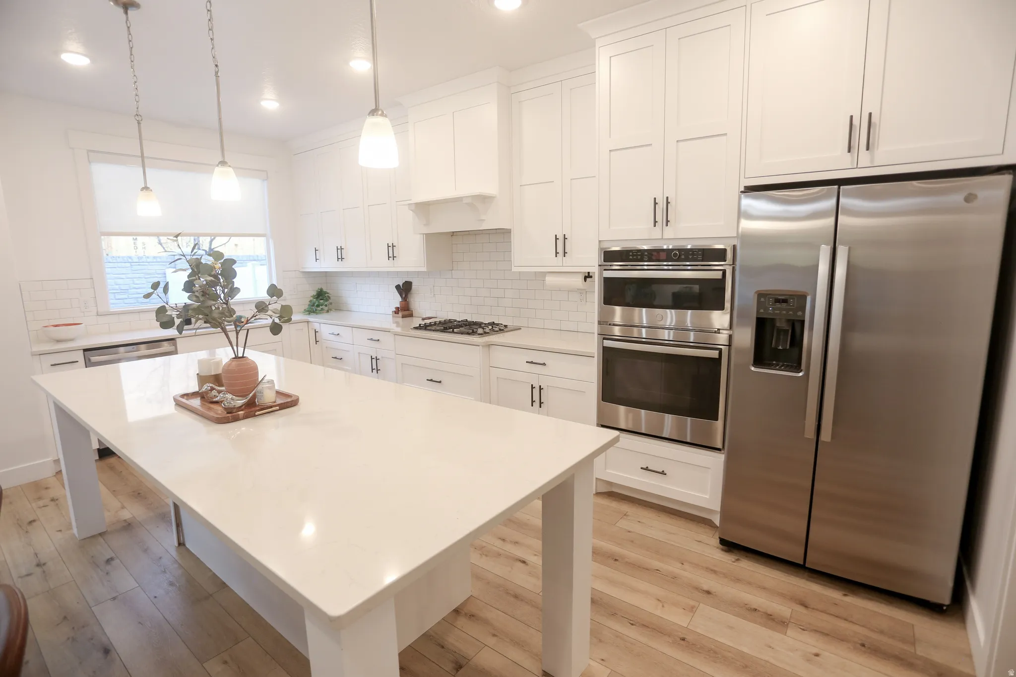 Kitchen with stainless steel appliances, white cabinets, light wood finished floors, and pendant lighting