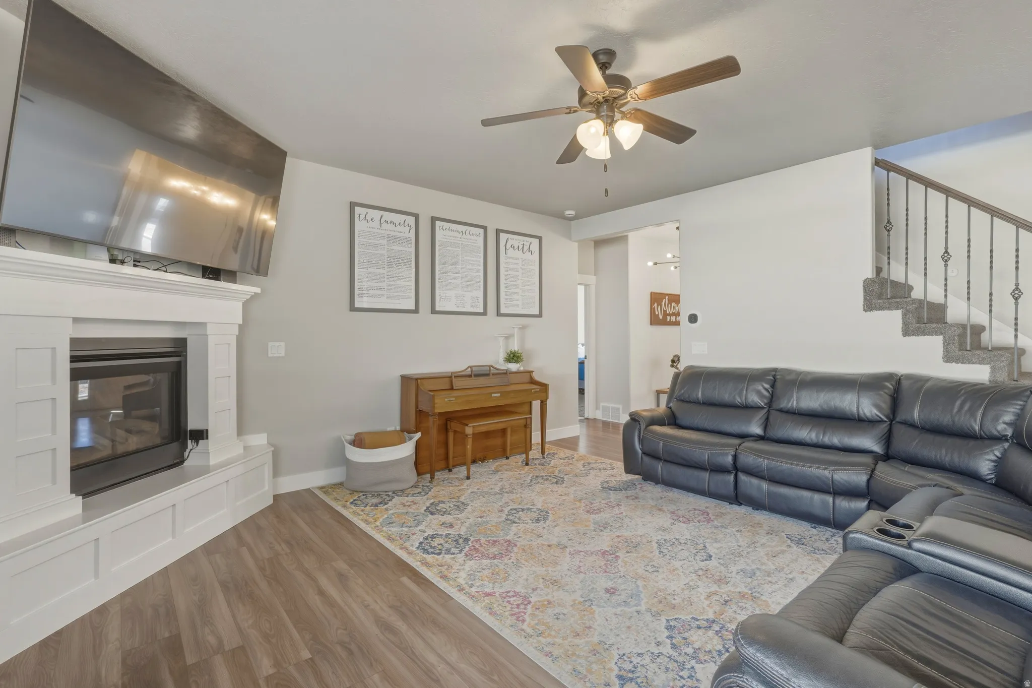Living room with wood finished floors, a ceiling fan, and a glass covered fireplace