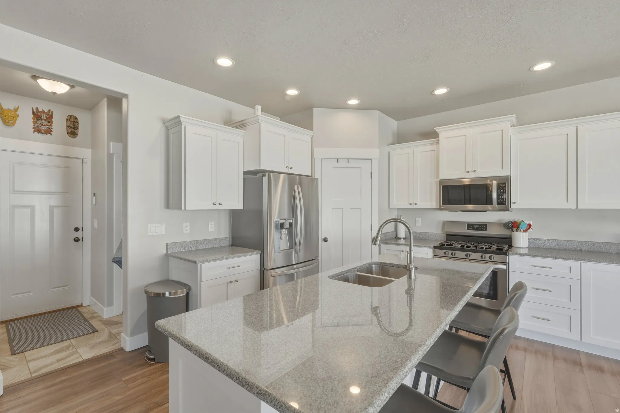 Kitchen with white cabinets, stainless steel appliances, light stone counters, a center island with sink, and recessed lighting