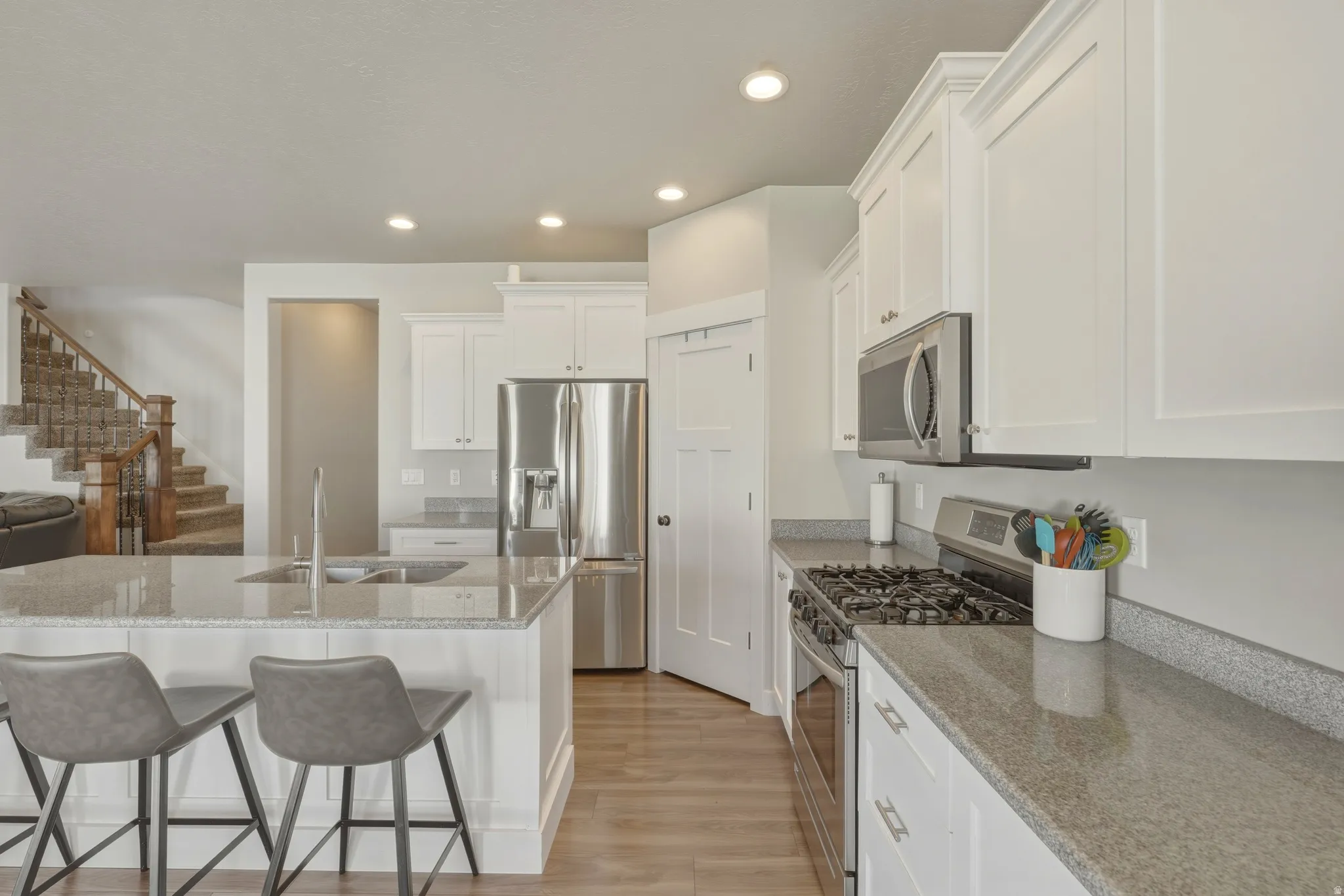 Kitchen with stainless steel appliances, light stone countertops, white cabinets, light wood-style flooring, and recessed lighting
