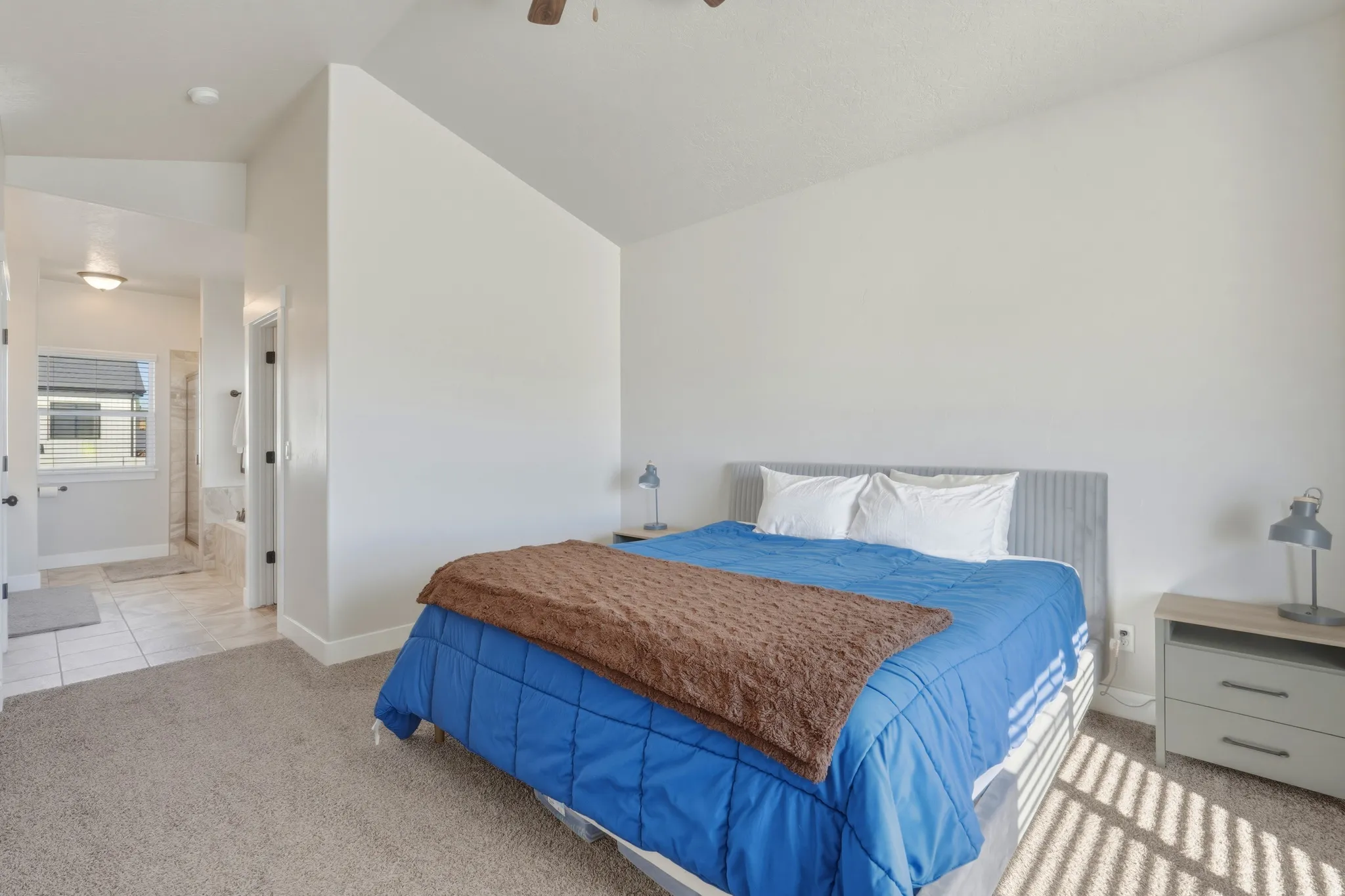Bedroom featuring light carpet, lofted ceiling, ensuite bathroom, and a ceiling fan